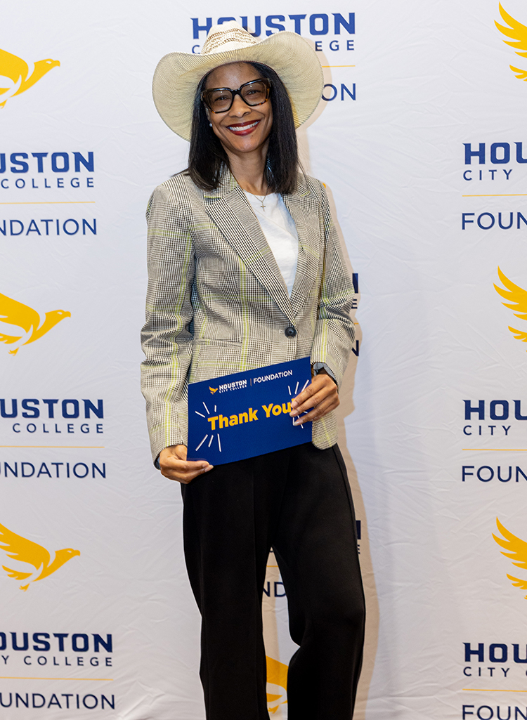 Attendee posing with a &ldquo;Thank You&rdquo; card in front of a Houston City College Foundation step-and-repeat backdrop at the Scholarship Luncheon.