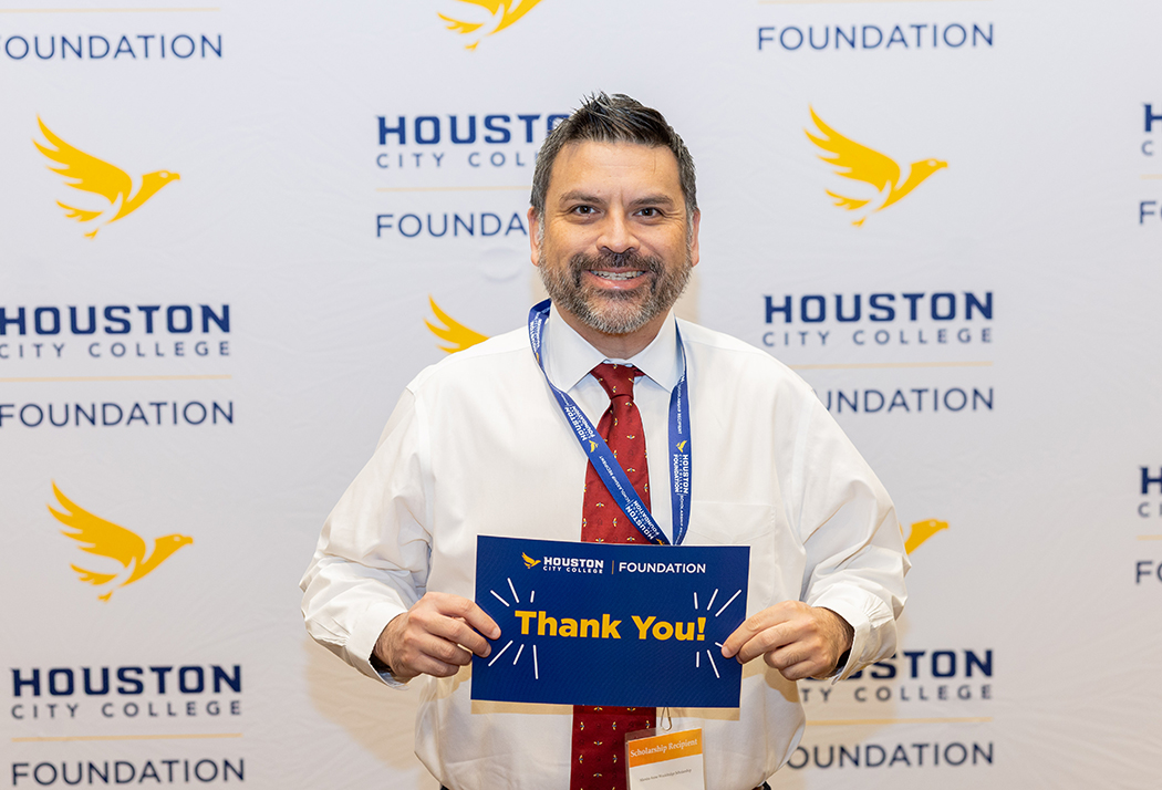 HCC Student Scholarship recipient holding a &ldquo;Thank You&rdquo; card in front of a HCC Foundation step-and-repeat branded backdrop at the Scholarship Luncheon.