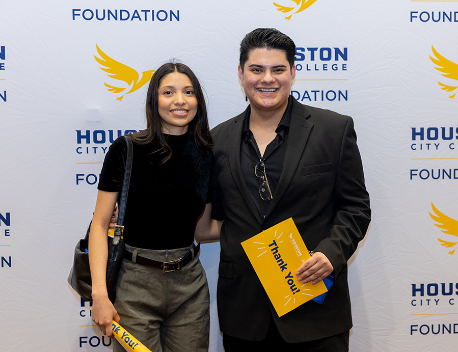 Two attendees posing together with a &ldquo;Thank You&rdquo; card in front of a HCC Foundation step-and-repeat backdrop at the Scholarship Luncheon.